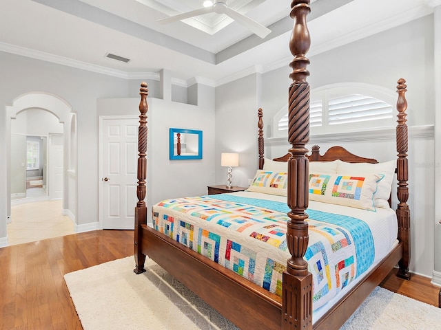 bedroom with arched walkways, ornamental molding, wood finished floors, and visible vents