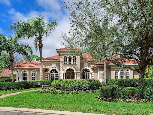 mediterranean / spanish home featuring a tiled roof, a front lawn, and stucco siding