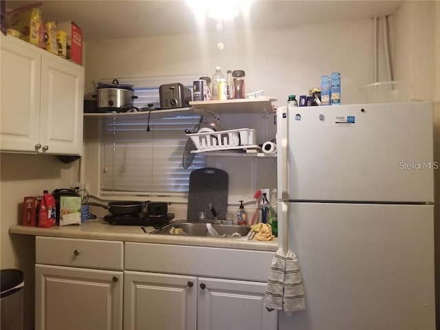 kitchen featuring a sink, white cabinets, light countertops, freestanding refrigerator, and open shelves