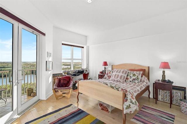 bedroom with access to outside, multiple windows, light wood-type flooring, and a water view