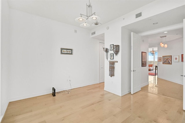 empty room with a chandelier, light wood-style flooring, and visible vents