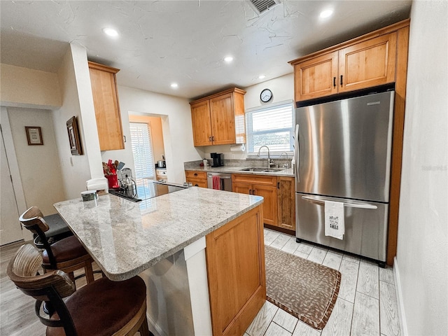 kitchen featuring a breakfast bar area, stainless steel appliances, a sink, light stone countertops, and light wood-type flooring