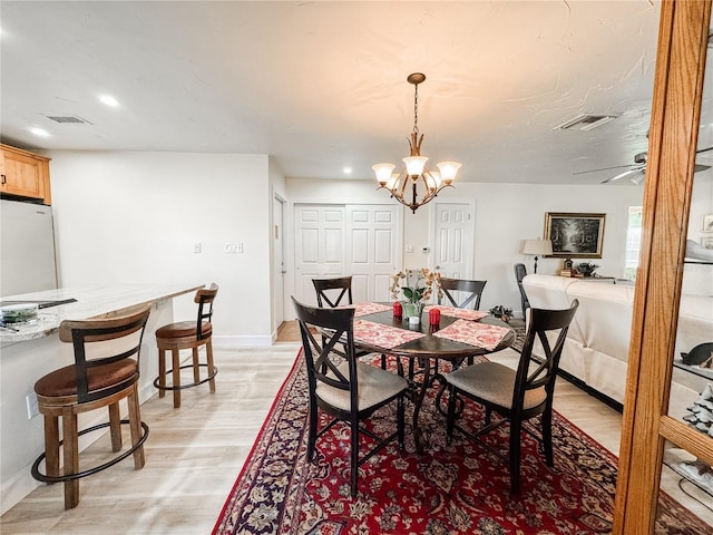 dining area with light wood-type flooring, visible vents, baseboards, and ceiling fan with notable chandelier