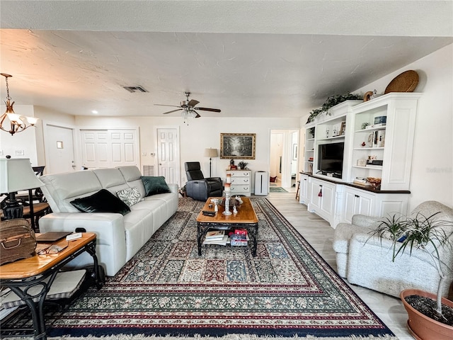 living area featuring a textured ceiling, ceiling fan with notable chandelier, wood finished floors, and visible vents