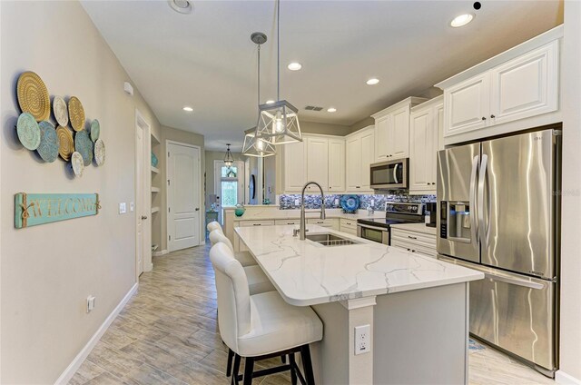 11607 Meadowgate Pl, Bradenton, FL 34211 - kitchen featuring a breakfast bar area, light stone countertops, light wood finished floors, a sink, and appliances with stainless steel finishes