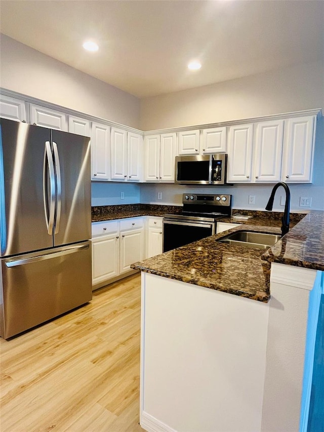 kitchen featuring light wood-style flooring, a peninsula, a sink, white cabinets, and appliances with stainless steel finishes