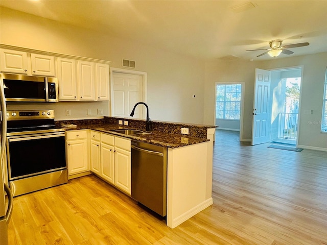 kitchen featuring appliances with stainless steel finishes, dark stone counters, white cabinetry, and a sink