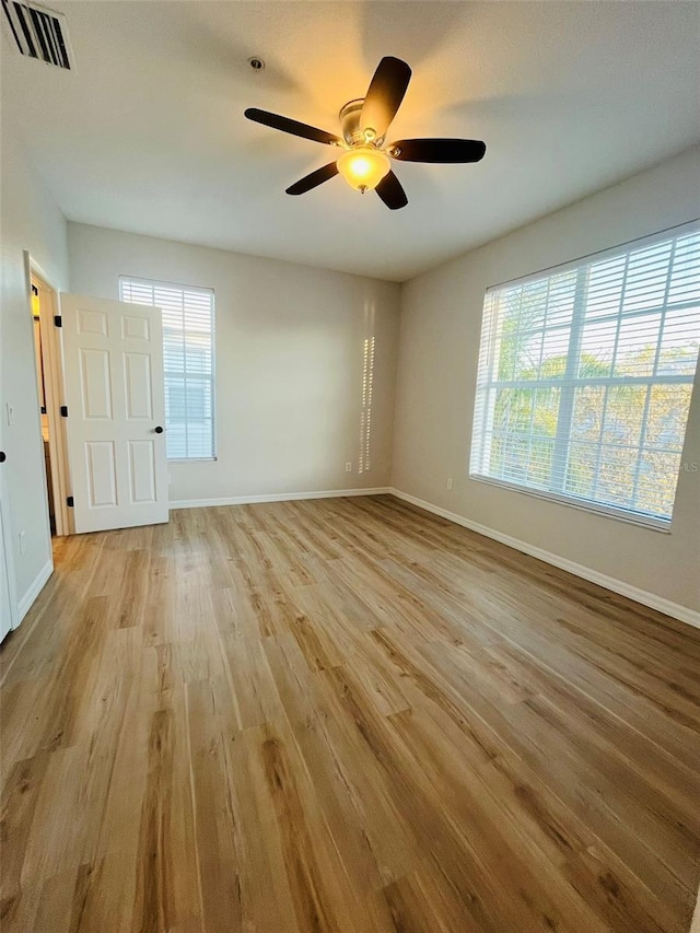 unfurnished room with light wood-style floors, a healthy amount of sunlight, visible vents, and baseboards