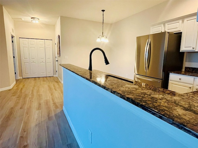 kitchen featuring white cabinets, light wood-type flooring, freestanding refrigerator, dark stone counters, and pendant lighting