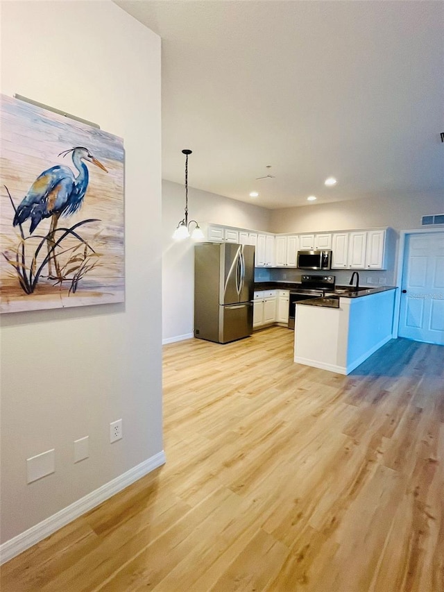 kitchen featuring pendant lighting, dark countertops, appliances with stainless steel finishes, light wood-style floors, and white cabinets