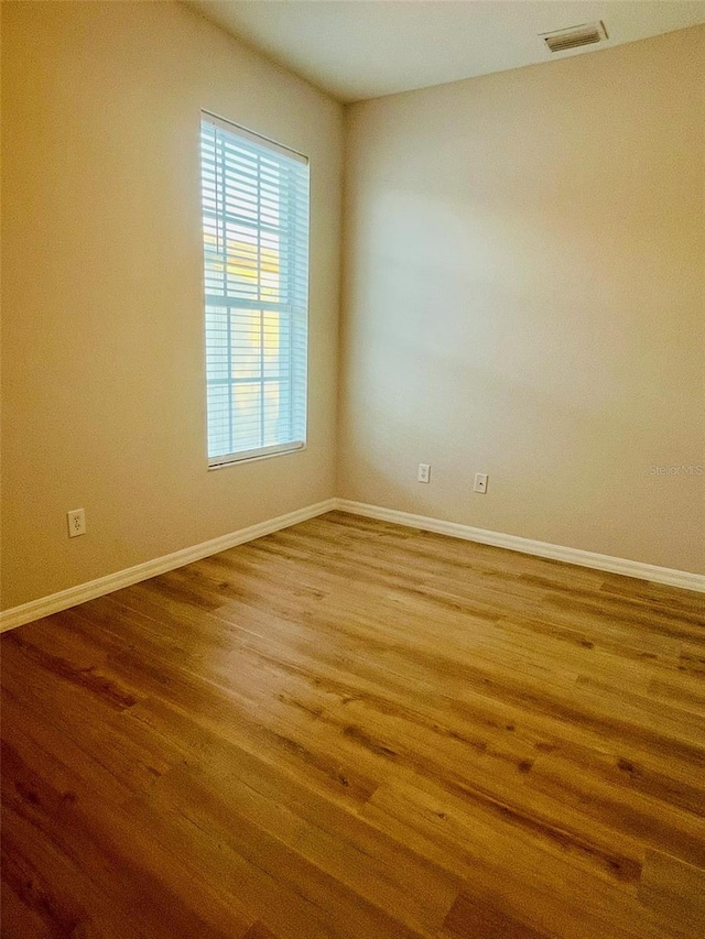 spare room with wood finished floors, visible vents, and baseboards