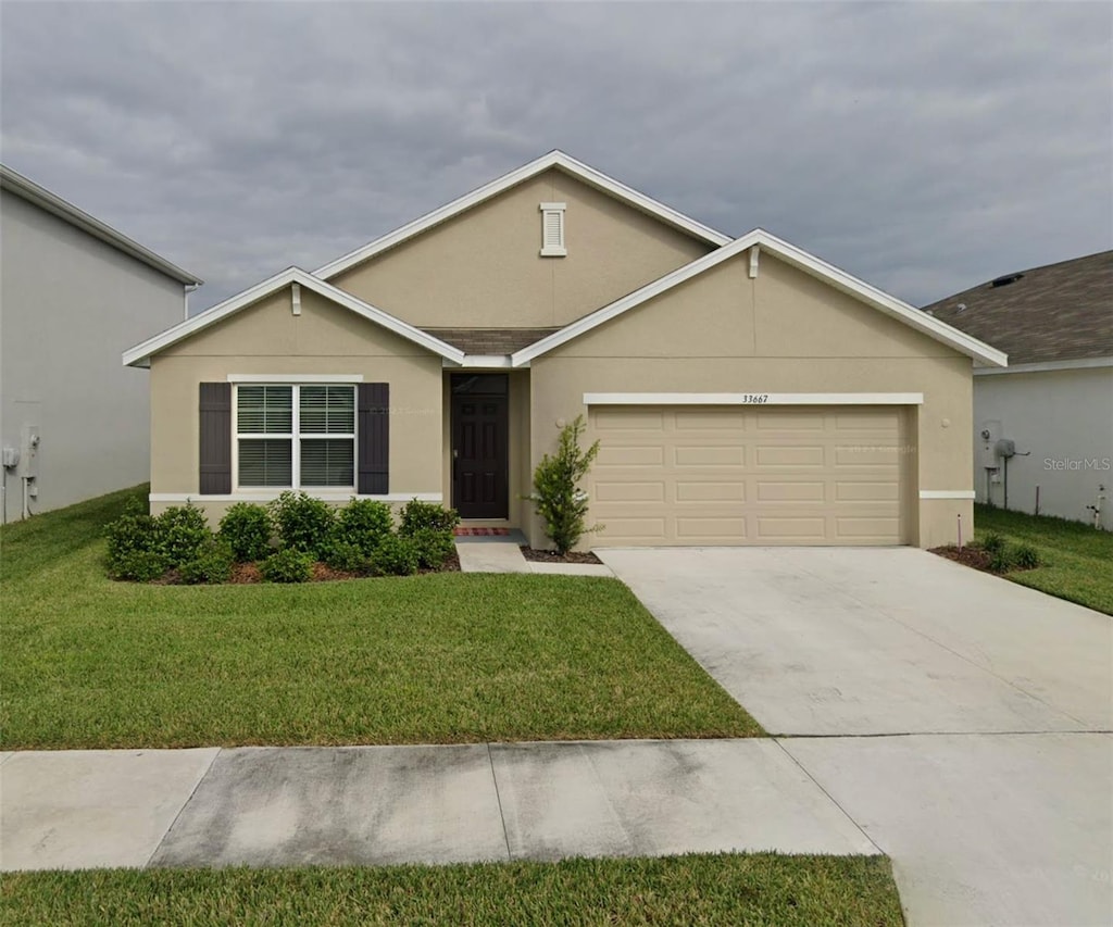 ranch-style house with stucco siding, a garage, concrete driveway, and a front lawn