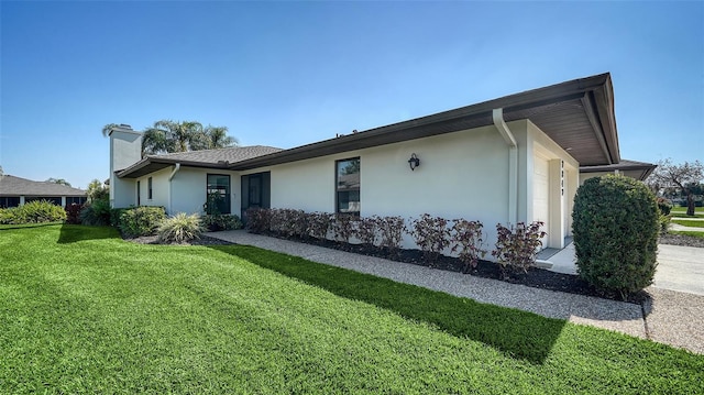 view of side of property featuring a lawn, a chimney, an attached garage, and stucco siding