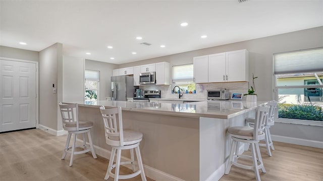 kitchen with decorative backsplash, a breakfast bar, stainless steel appliances, light wood-type flooring, and white cabinetry