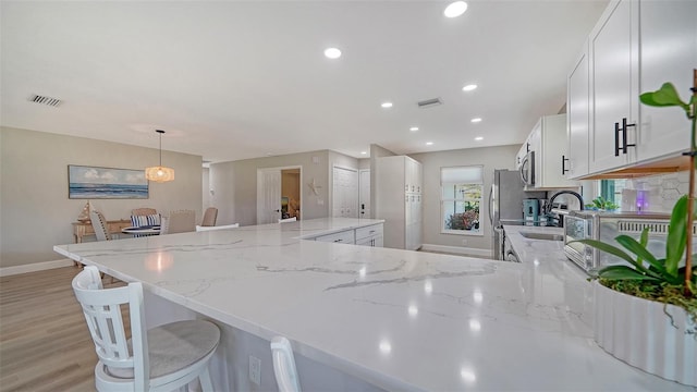 kitchen featuring stainless steel appliances, a sink, visible vents, light wood-style floors, and white cabinetry