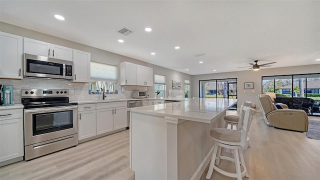 kitchen featuring stainless steel appliances, visible vents, white cabinetry, open floor plan, and a kitchen bar