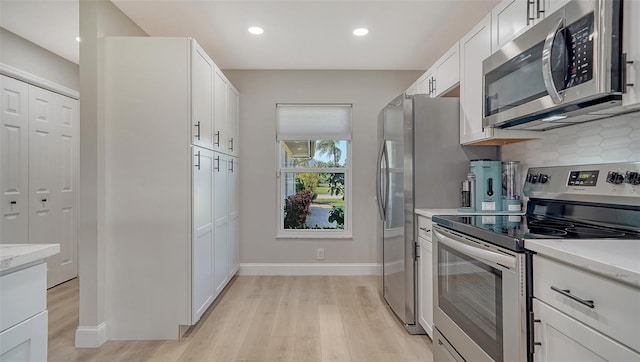 kitchen featuring white cabinets, light stone counters, stainless steel appliances, light wood-style floors, and backsplash