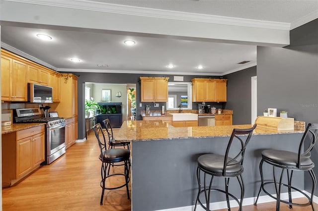 kitchen featuring light wood finished floors, visible vents, ornamental molding, a kitchen breakfast bar, and stainless steel appliances