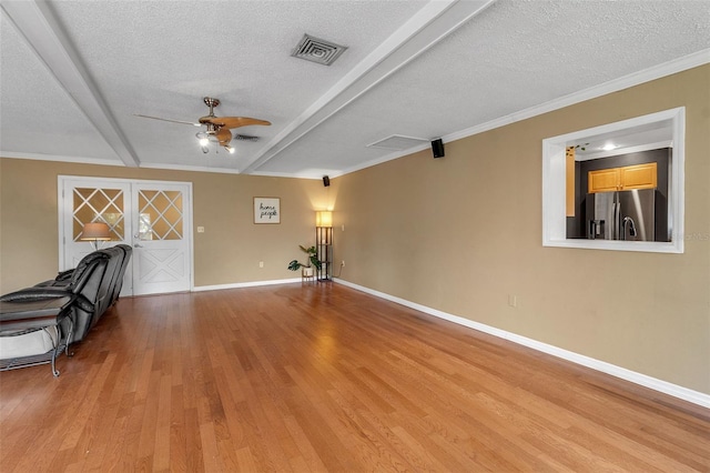 interior space featuring ceiling fan, a textured ceiling, baseboards, light wood-style floors, and beamed ceiling