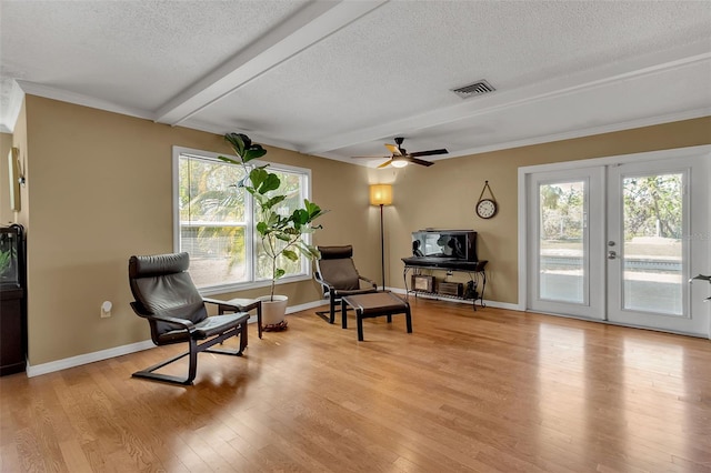 living area featuring beam ceiling, visible vents, light wood-style flooring, and a textured ceiling