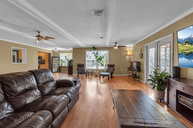 living area featuring visible vents, baseboards, ornamental molding, a textured ceiling, and light wood-type flooring