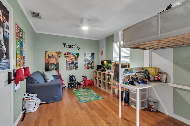 rec room featuring ceiling fan, wood finished floors, visible vents, baseboards, and crown molding