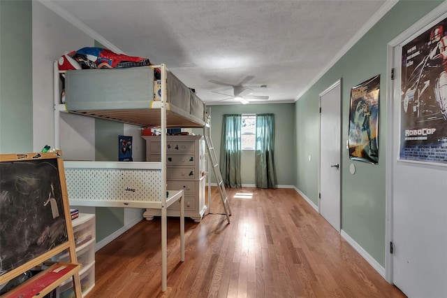 bedroom featuring a textured ceiling, ornamental molding, wood finished floors, and baseboards