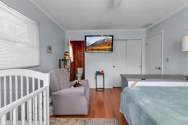 bedroom featuring wood finished floors, visible vents, a closet, a nursery area, and crown molding