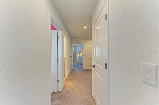 hallway featuring light carpet and a textured wall