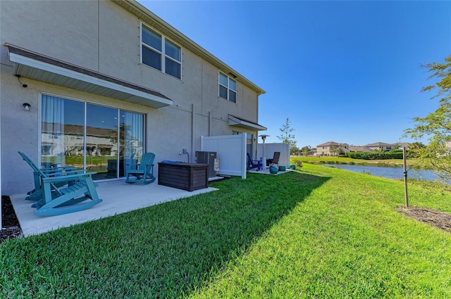 back of house featuring a water view, a patio area, a lawn, and stucco siding