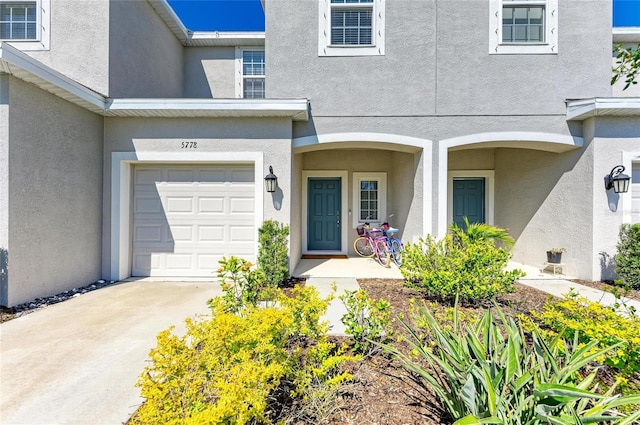 doorway to property with an attached garage, concrete driveway, and stucco siding