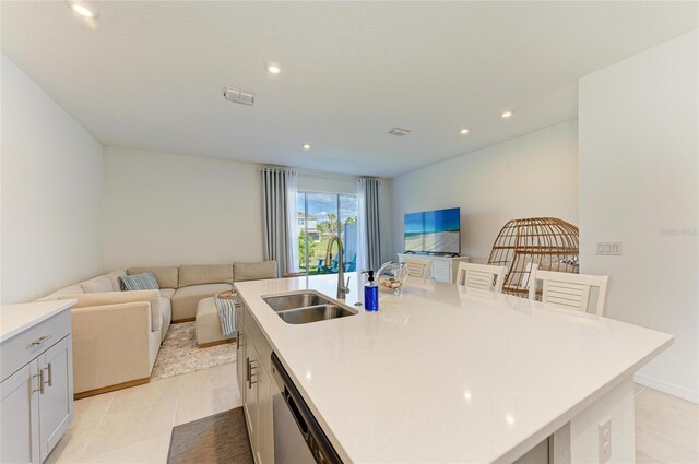 kitchen featuring light countertops, stainless steel dishwasher, open floor plan, a sink, and an island with sink