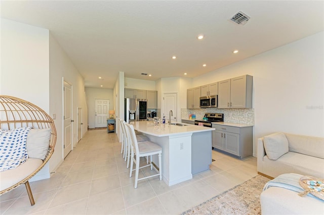 kitchen featuring a breakfast bar area, tasteful backsplash, gray cabinets, appliances with stainless steel finishes, and a sink