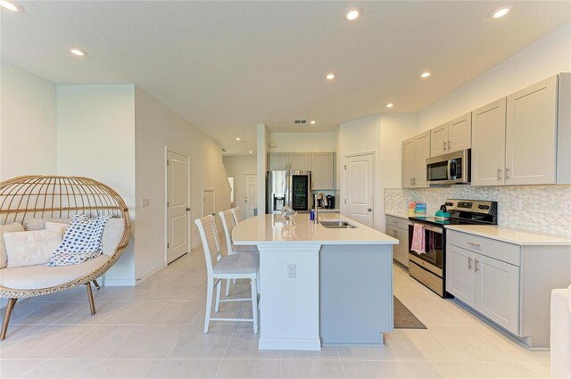 kitchen with backsplash, gray cabinetry, appliances with stainless steel finishes, a kitchen island with sink, and a sink