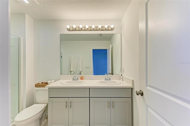 bathroom featuring toilet, double vanity, a textured ceiling, and a sink