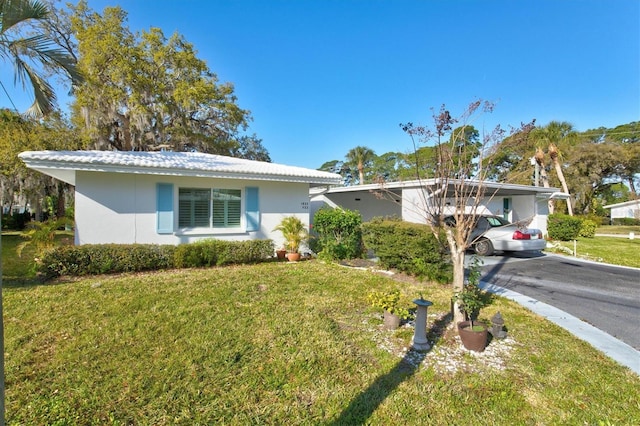 ranch-style home with driveway, stucco siding, a carport, and a front yard