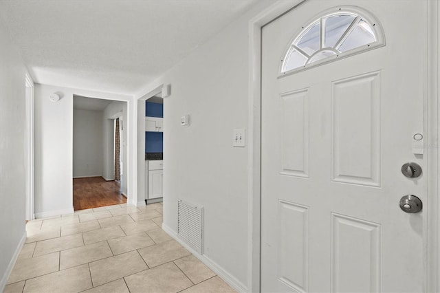 entryway featuring visible vents, a textured ceiling, baseboards, and light tile patterned flooring