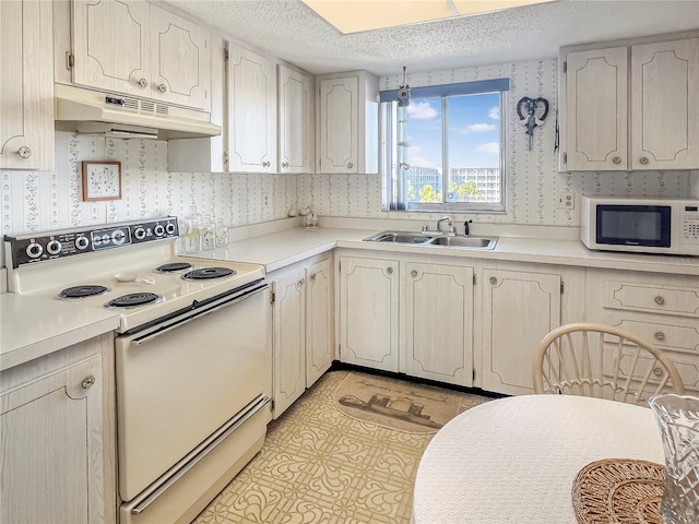 kitchen with a sink, a textured ceiling, white appliances, under cabinet range hood, and wallpapered walls