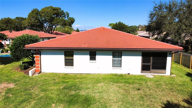 back of property featuring fence, a lawn, a tiled roof, and stucco siding