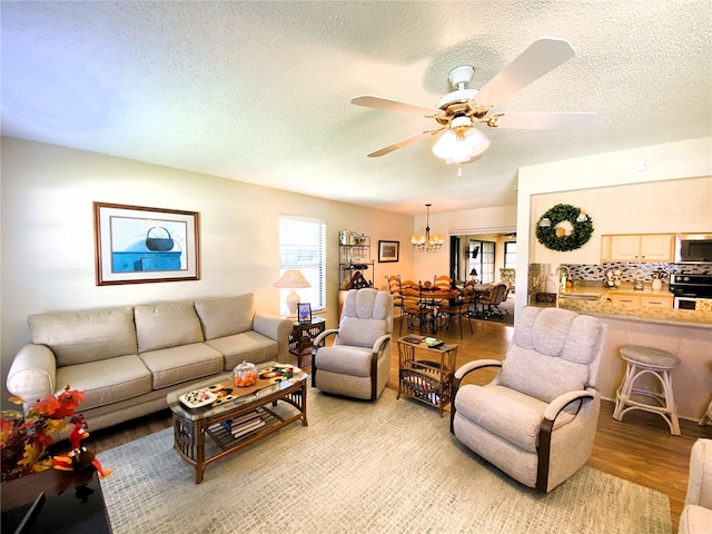 living room with light wood finished floors, a textured ceiling, and ceiling fan with notable chandelier