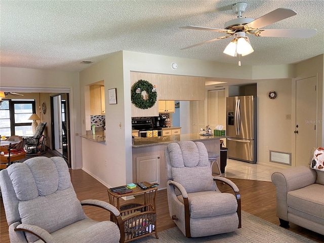 living room with light wood-style floors, a textured ceiling, visible vents, and a ceiling fan