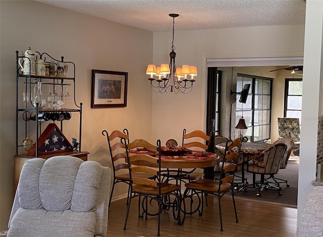 dining room with ceiling fan with notable chandelier, a textured ceiling, and wood finished floors