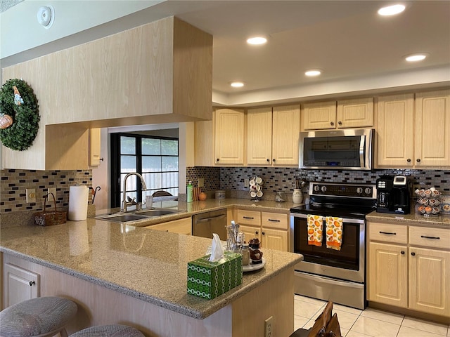 kitchen with light tile patterned floors, stainless steel appliances, a peninsula, a sink, and a kitchen bar