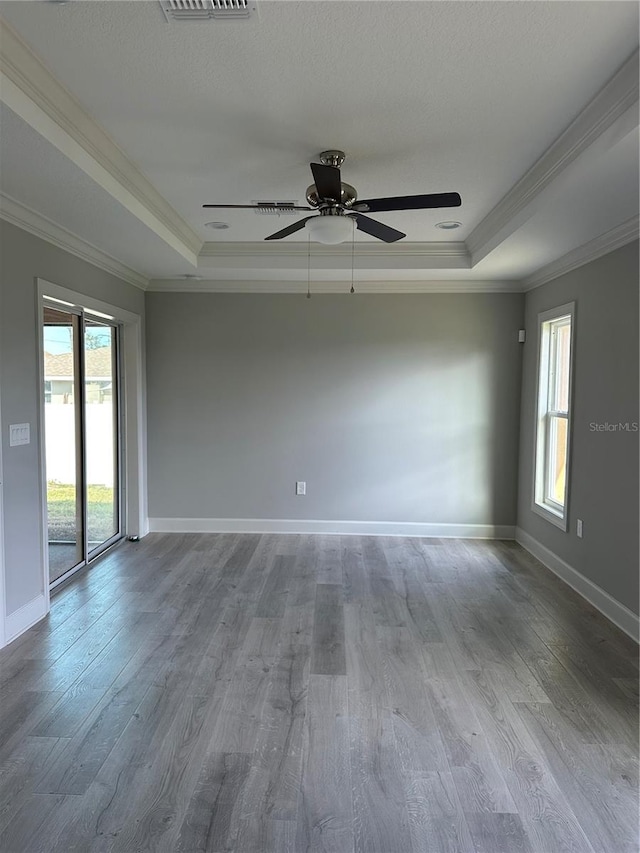 empty room with baseboards, crown molding, a tray ceiling, and wood finished floors