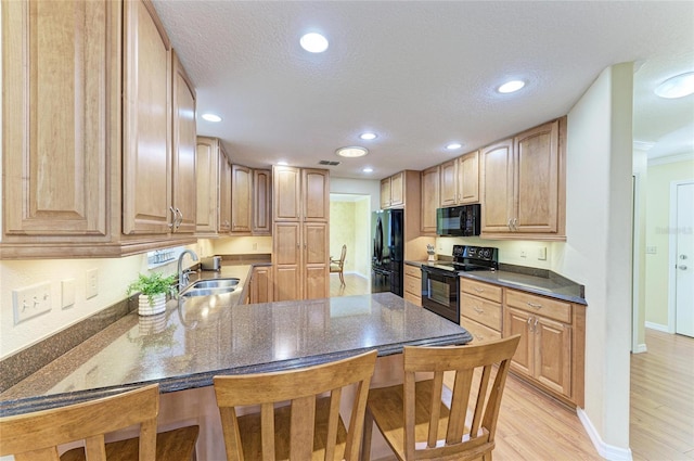 kitchen featuring light wood-style floors, a breakfast bar, a sink, and black appliances