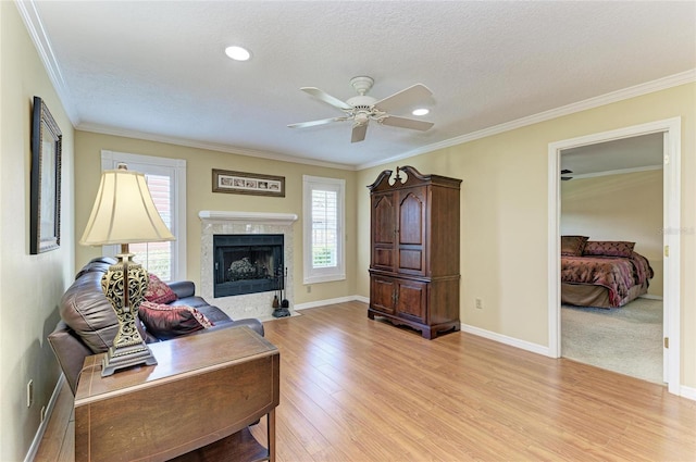 living room featuring baseboards, a textured ceiling, crown molding, light wood-style floors, and a fireplace