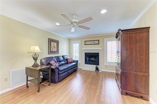 living room featuring light wood finished floors, visible vents, ornamental molding, a ceiling fan, and baseboards