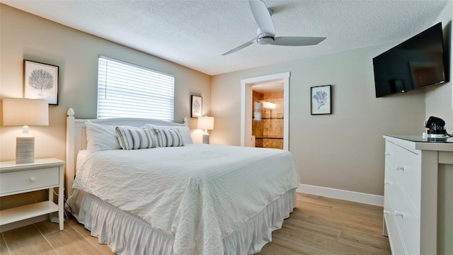 bedroom featuring a ceiling fan, baseboards, light wood finished floors, ensuite bathroom, and a textured ceiling