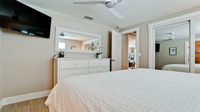 bedroom featuring a ceiling fan, baseboards, wood finished floors, visible vents, and a textured ceiling