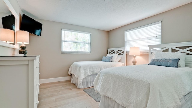 bedroom featuring baseboards, a textured ceiling, and light wood-style flooring